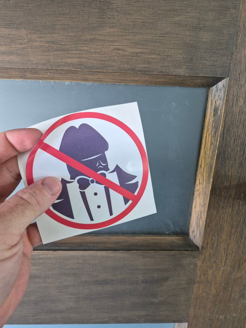 Hand holding a No Dickheads Allowed  sticker against a wooden background