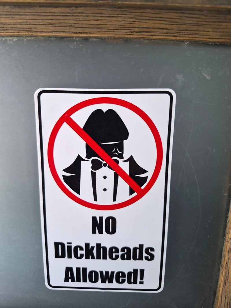 Sign with a humorous 'No Dickheads Allowed!' Sticker on a chalkboard background