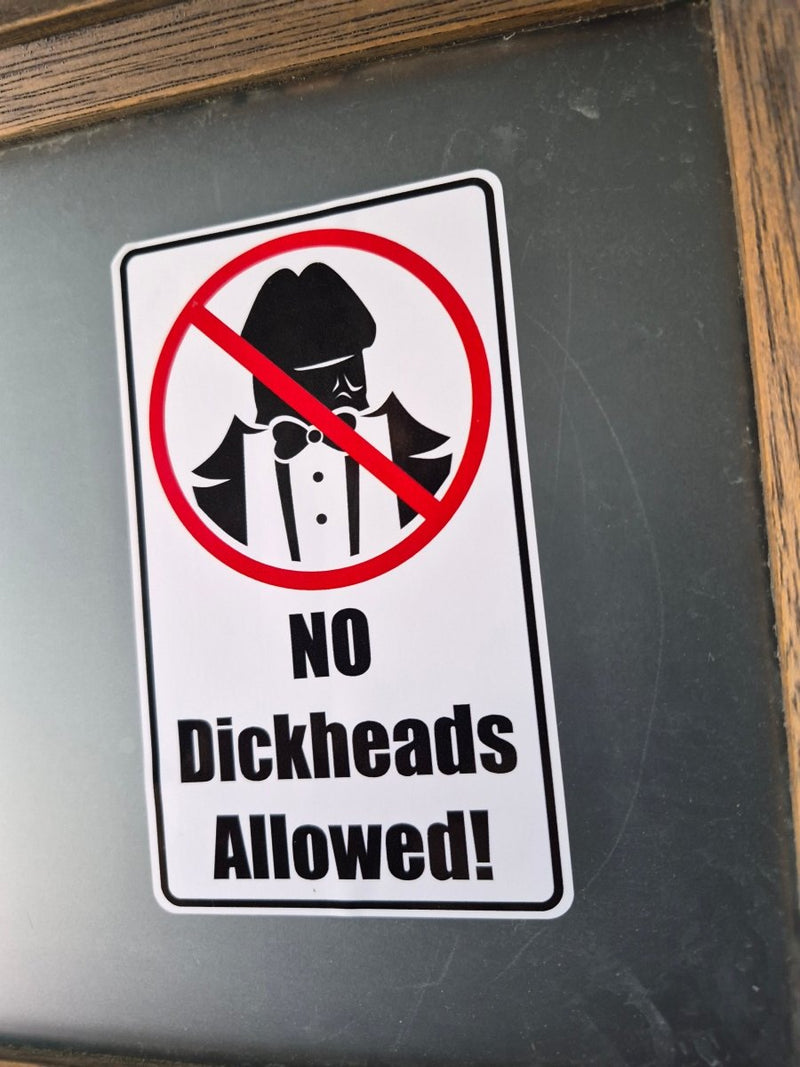Sticker with a 'No dickheads allowed!' message on a metallic surface.