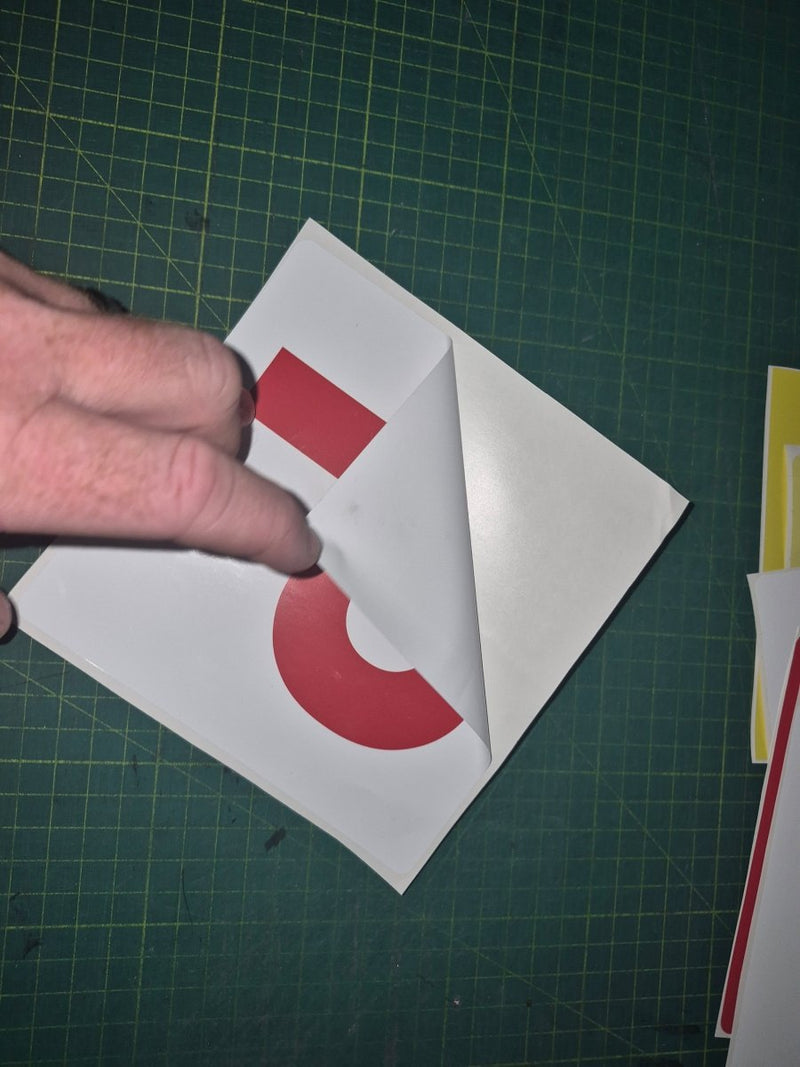 Hand folding a piece of vinyl sticker with a red circle on a green cutting mat.