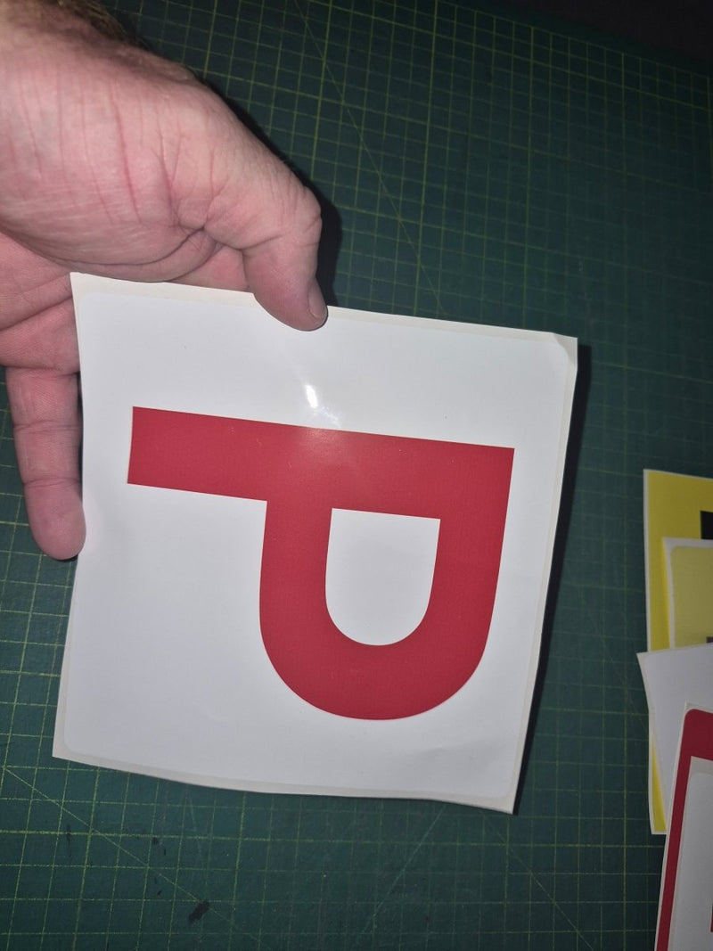Hand holding a red 'P' on a white background against a green cutting mat.