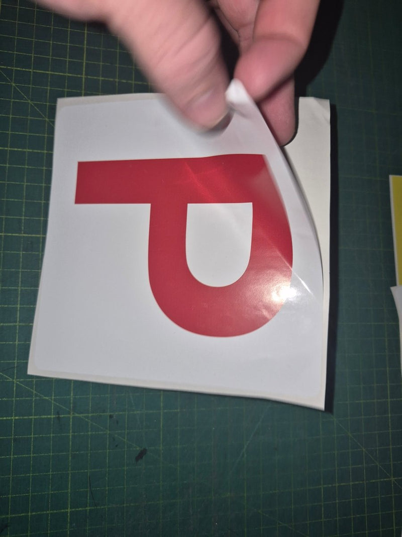 Red 'P' sticker held over a white square on a green cutting mat.