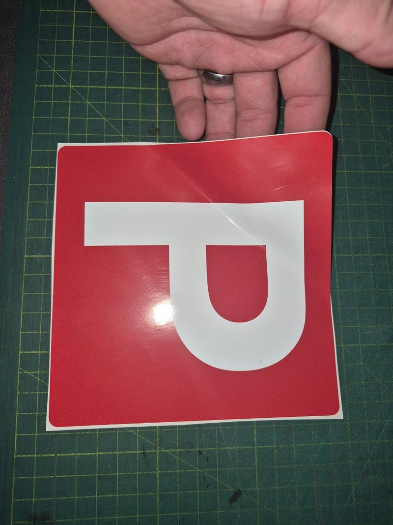 Red square sign with a white 'P' held by a hand on a green cutting mat.