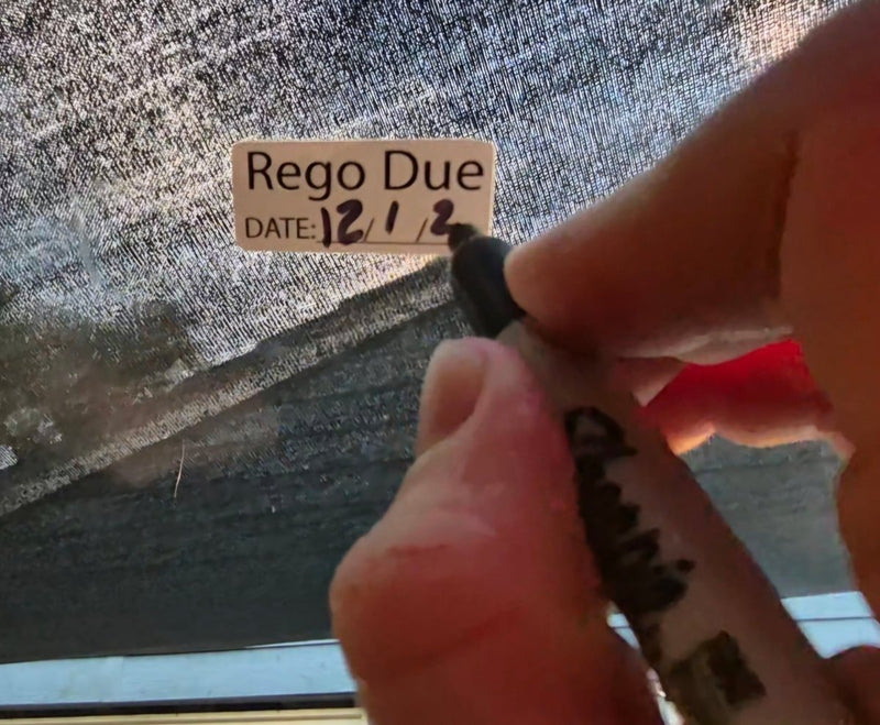Hand holding a marker near a 'Rego Due' sign on a textured surface