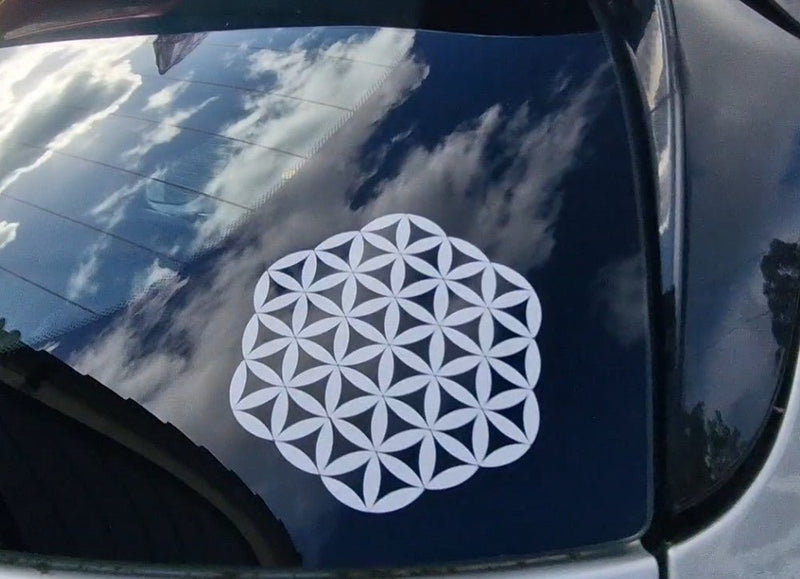 White flower of life symbol on a car window with a blue sky reflection.