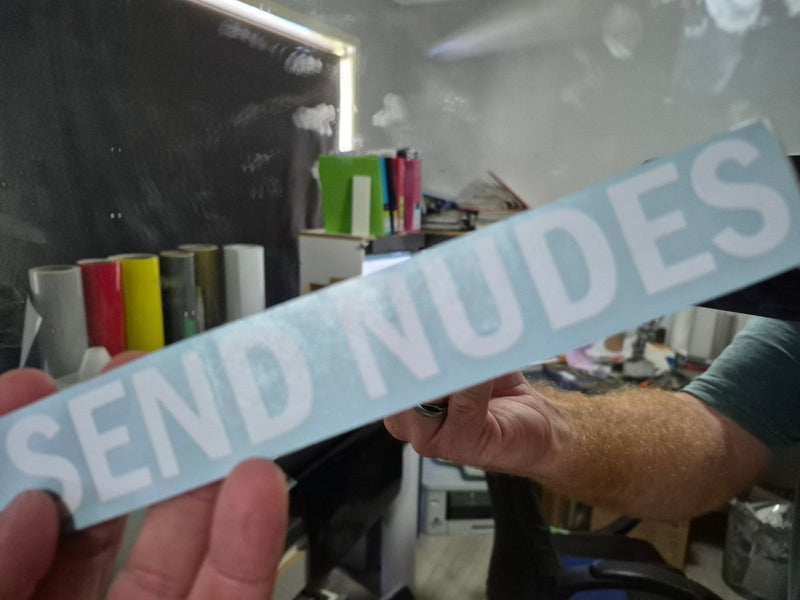 Person holding a vinyl decal with 'SEND NUDES' text in an indoor setting.