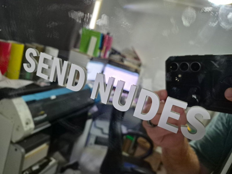 Person holding a phone with 'SEND NUDES' text in a room with equipment and supplies.