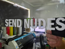 Load image into Gallery viewer, Person holding a sign with 'SEND NUDES' in a room with printing equipment.
