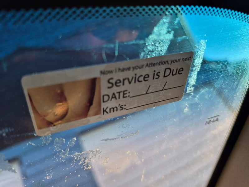 Service due date label on a car windshield with water droplets.