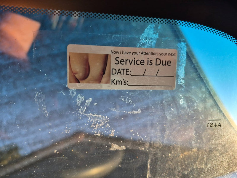 Service due date sticker on a car windshield with a blurred background