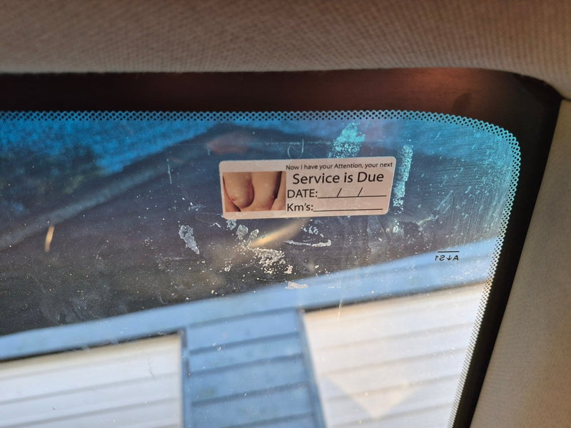 Car windshield with a service due reminder sticker on a blurred background