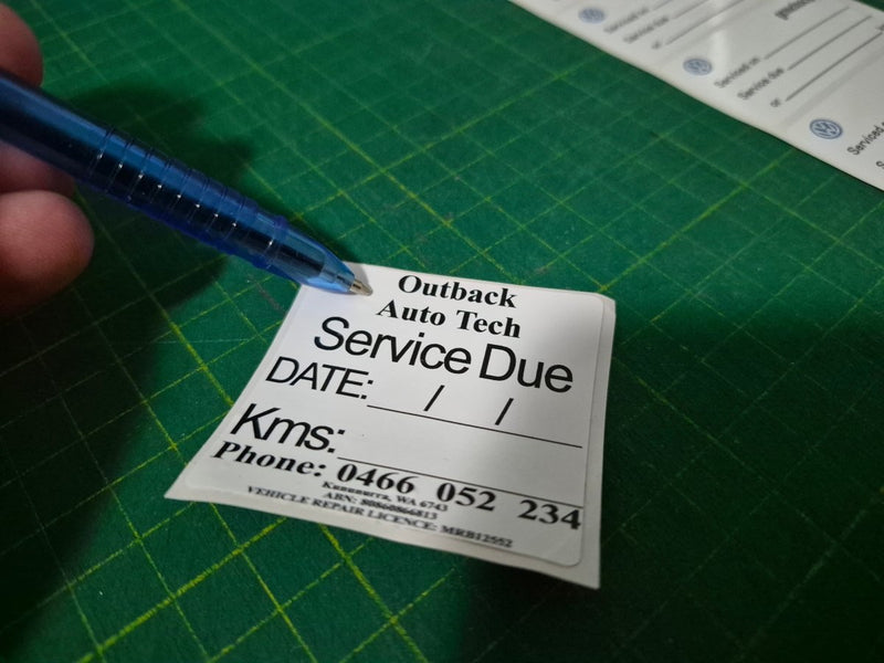 Service due label held by a hand with a pen on a green cutting mat