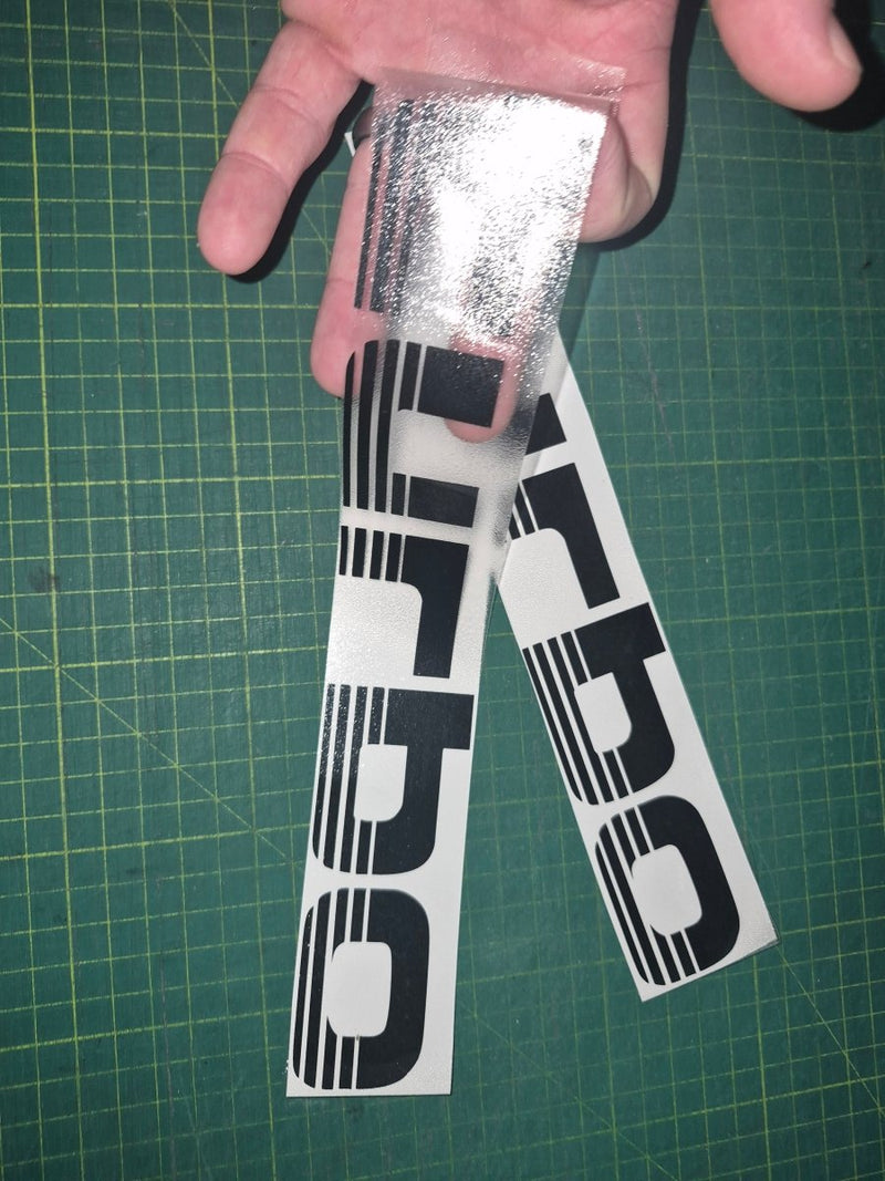 Two 'Turbo' decals being held over a green cutting mat.
