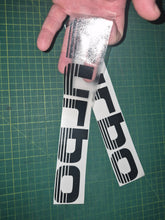 Load image into Gallery viewer, Two 'Turbo' decals being held over a green cutting mat.

