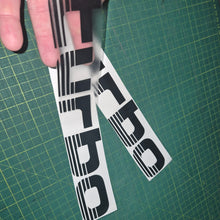 Load image into Gallery viewer, Two 'Turbo' decals held over a green cutting mat.
