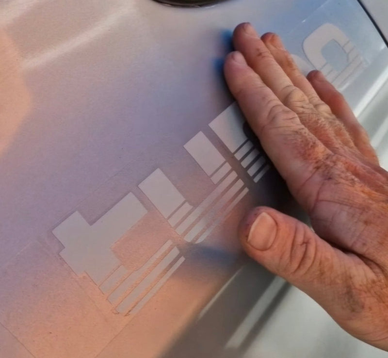 Hand touching a Silver tubro decals on white surface.