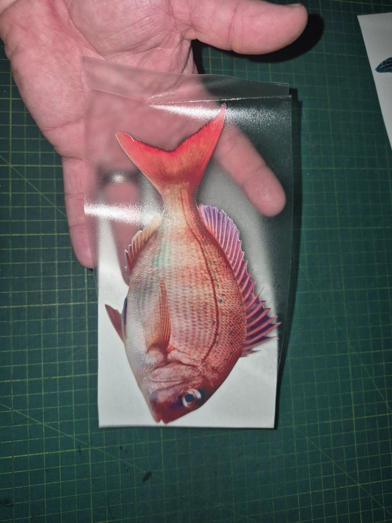 Hand holding a card with a red fish illustration on a green cutting mat.