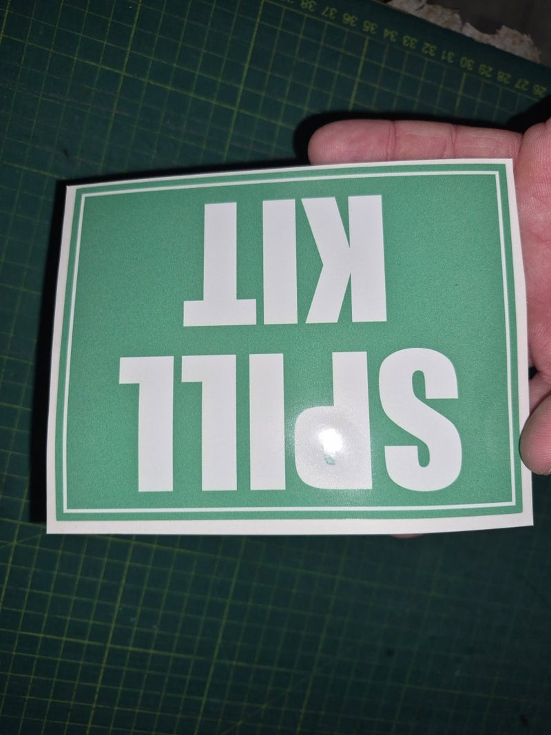Hand holding a green sign with 'SPILL KIT' text on a grid background