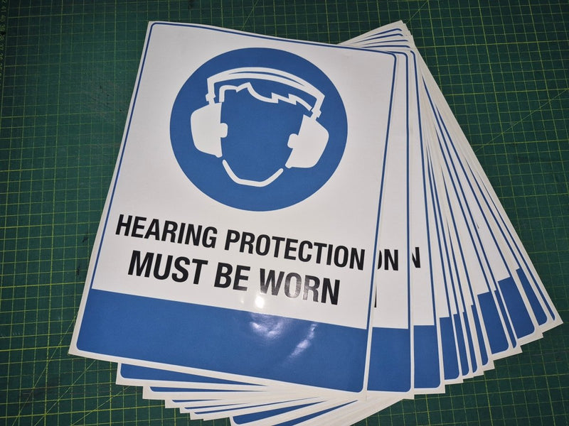Stack of 'Hearing Protection Must Be Worn' signs on a green grid background