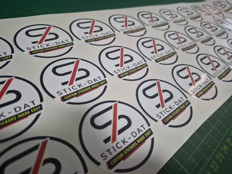 Sheet of Stick-Dat stickers with brand logo on a cutting mat.
