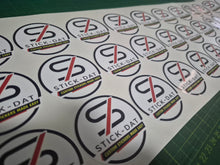 Load image into Gallery viewer, Sheet of Stick-Dat stickers with brand logo on a cutting mat.
