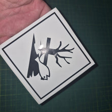 Load image into Gallery viewer, Sticker with a black silhouette of a tree and fish on a white background, held over a dark surface.
