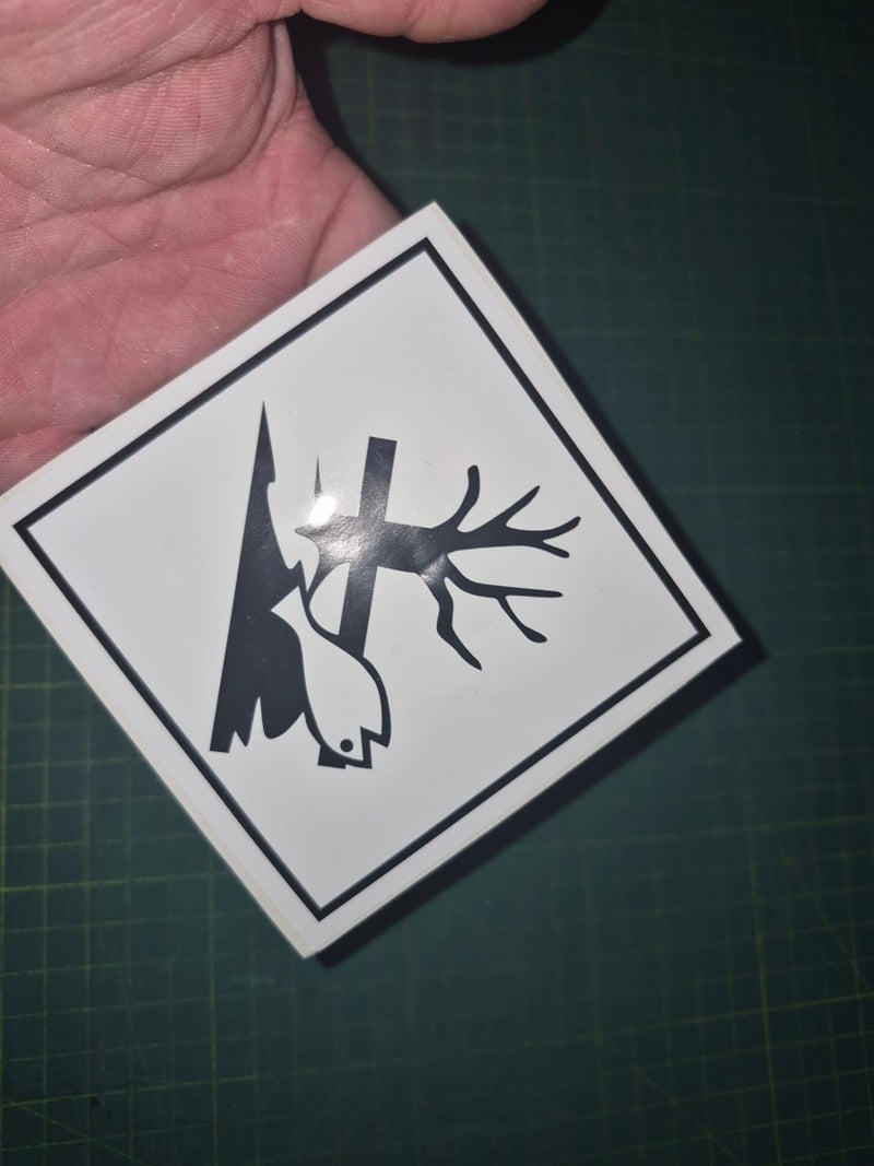 Sticker with a black silhouette of a tree and fish on a white background, held over a dark surface.