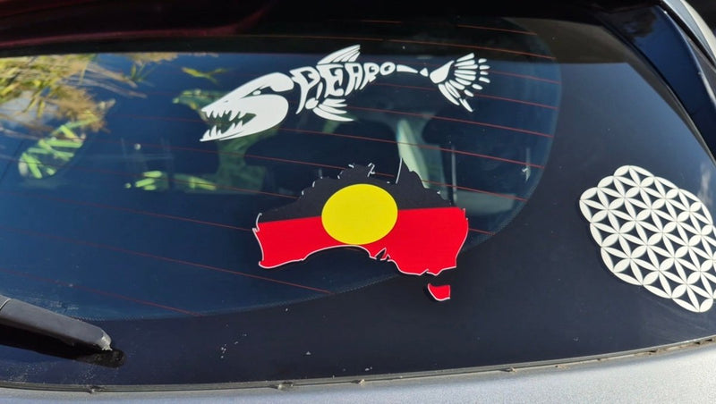 Car window with three decals: a white fish skeleton, an Aboriginal flag, and a geometric design.