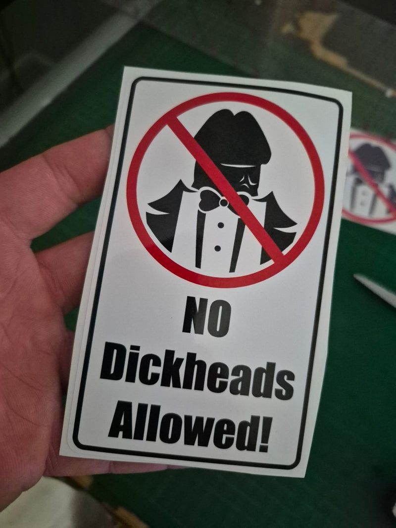 Sticker with a crossed-out face icon and 'No Dickheads Allowed!' text held by a hand.