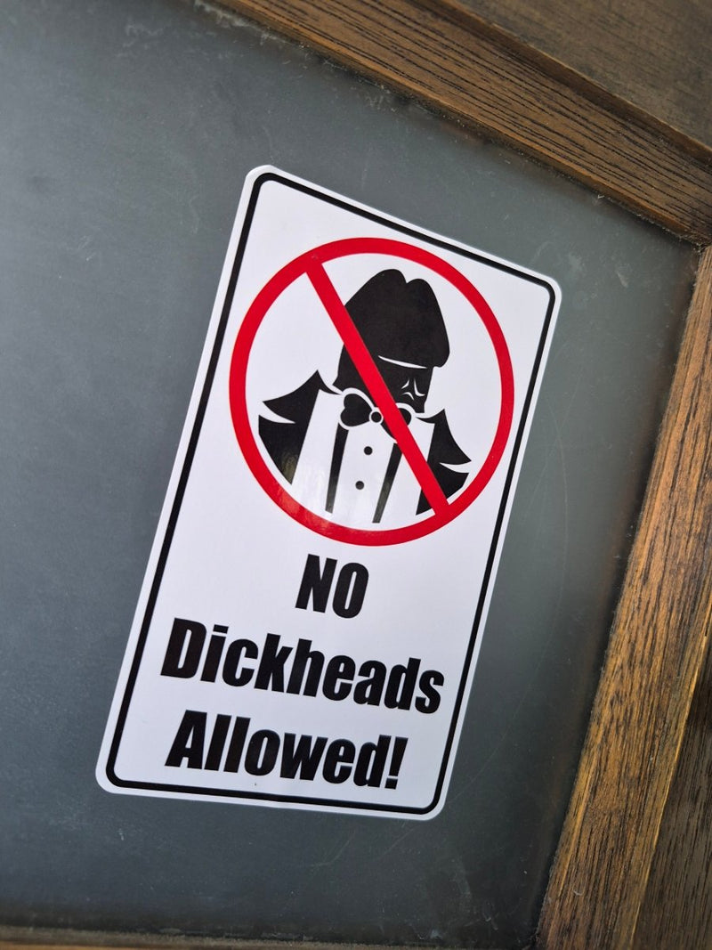 Sticker with a humorous message 'No Dickheads Allowed!' on a reflective surface.