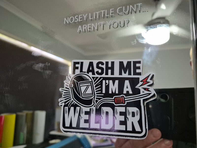 Sticker with text 'Flash me I'm a welder' held up to a mirror with text on it.