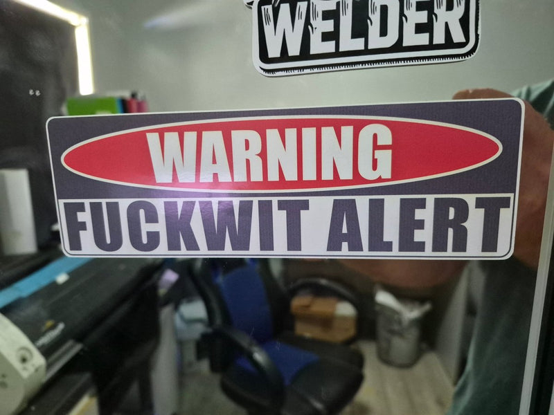 Warning sign with 'FUCKWIT ALERT' text on a blurred background