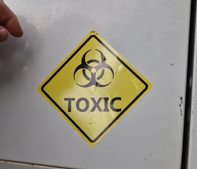 Toxic warning sign on a metallic surface with a hand partially visible.