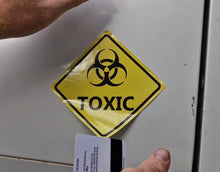 Load image into Gallery viewer, Yellow 'TOXIC' sign with biohazard symbol on a metallic surface.
