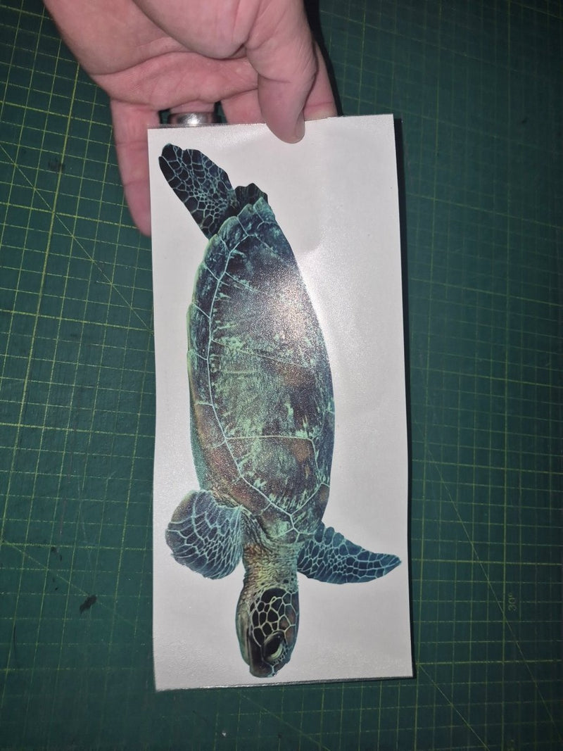 Hand holding a turtle decal on a cutting mat