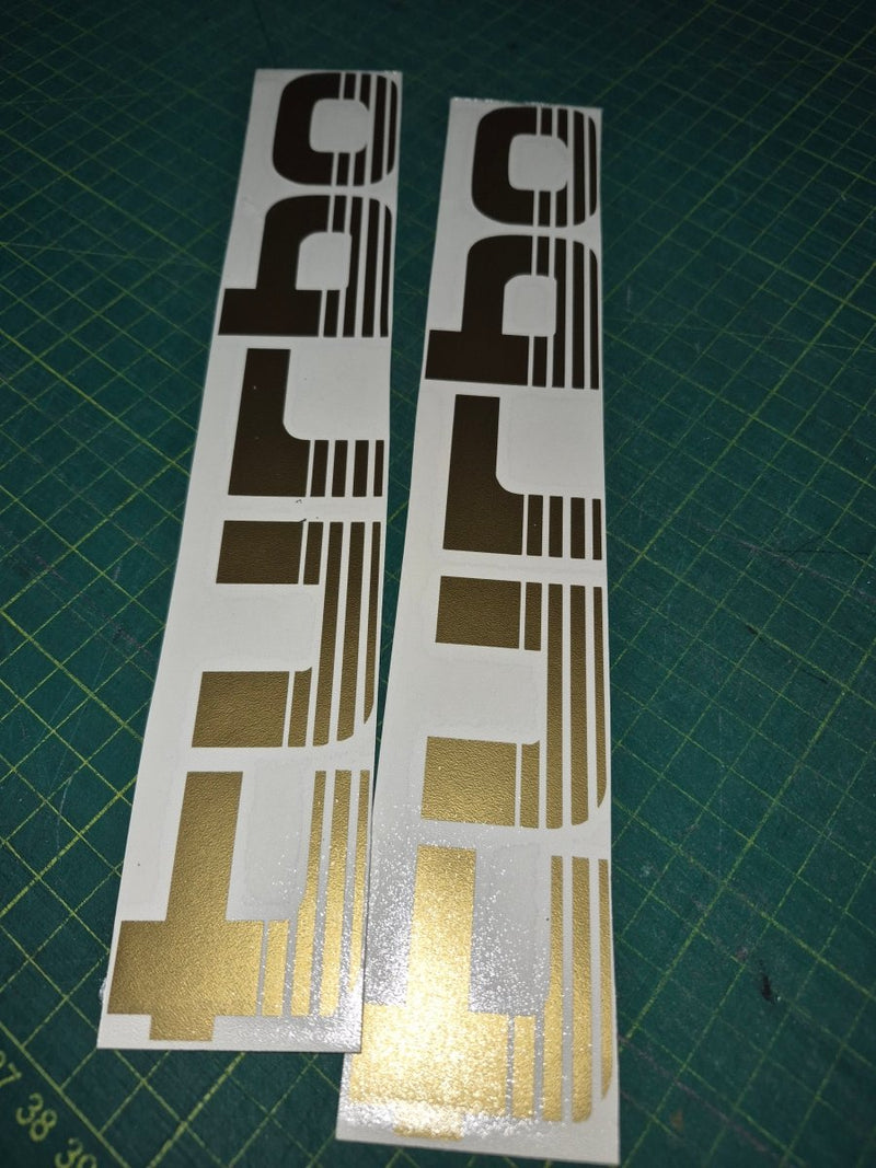 Two gold and black car decals on a green cutting mat.