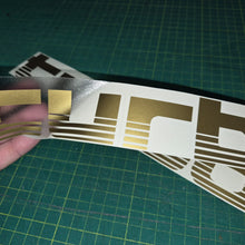 Load image into Gallery viewer, Gold and brown decal held over a larger decal on a green cutting mat.
