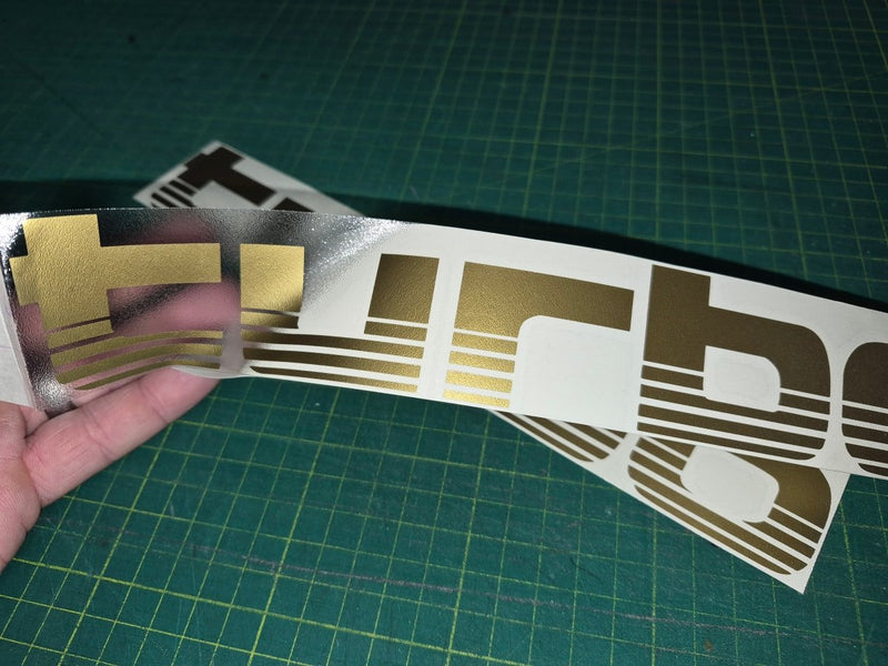 Gold and brown decal held over a larger decal on a green cutting mat.