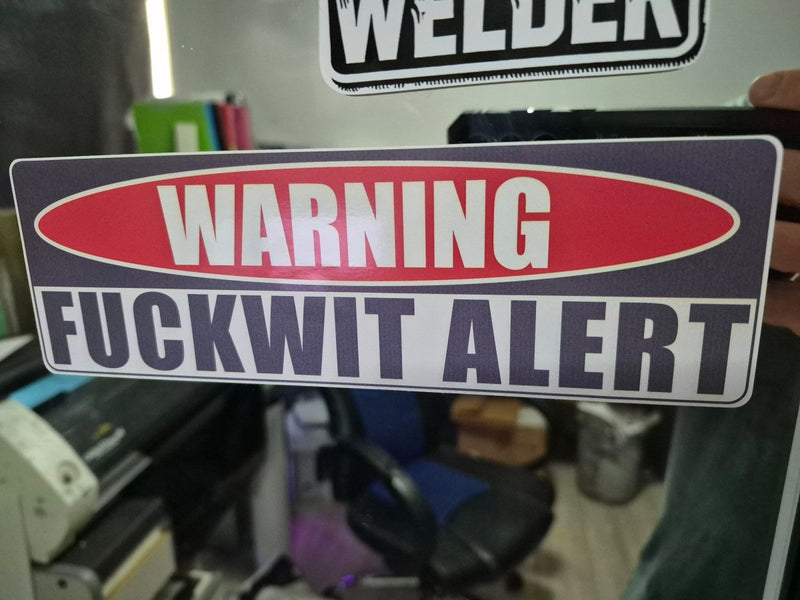 Warning sticker with 'FUCKWIT ALERT' text on a blurred background