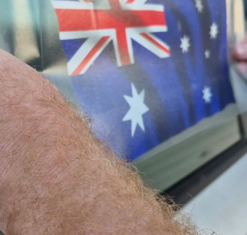 Close-up of a person applying an Australian flag in the background on a car window