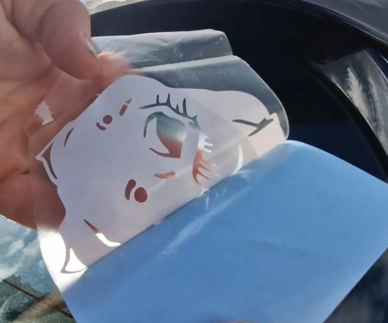 Hand holding a small plastic bag with a cartoon face design against a blurred outdoor background.