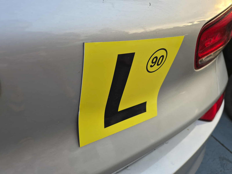Yellow L plate on a car's rear, indicating a learner driver 90kms design.