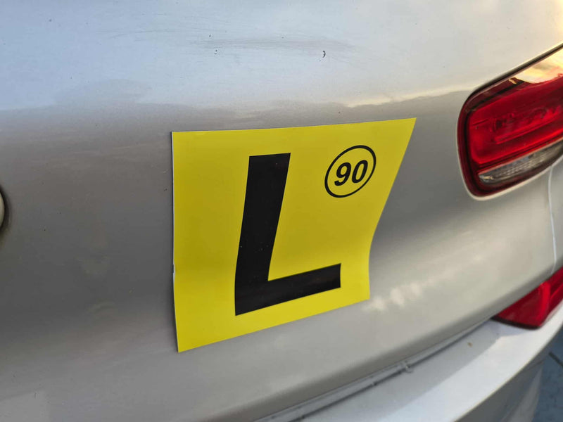 Yellow learner's magnet with a black 'L' on a car's rear.