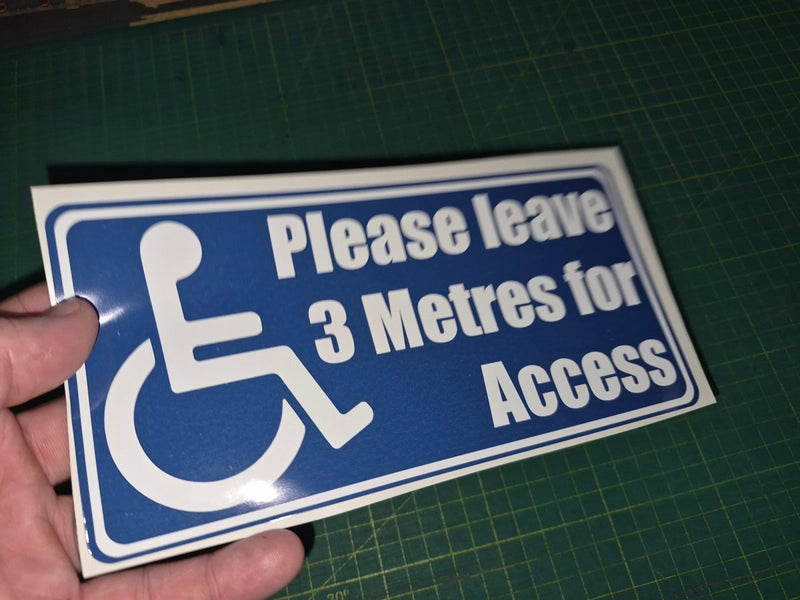 Handheld sign with wheelchair icon and text 'Please leave 3 Metres for Access' on a green cutting mat.