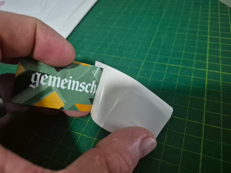 Hand holding doubled sided Service due sticker branding on a green cutting mat.