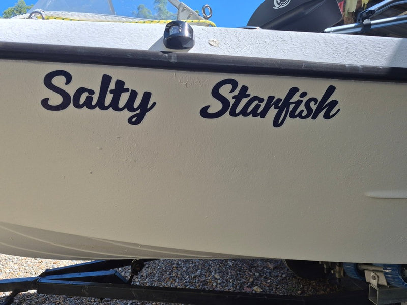 Beige boat with 'Salty Starfish' text on a gravel surface. custom Australian made boat stickers