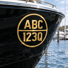 Load image into Gallery viewer, Gold cut-vinyl round boat registration decal on a black hull
