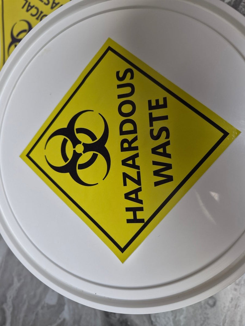 White container with a yellow hazardous waste label featuring a biohazard symbol.