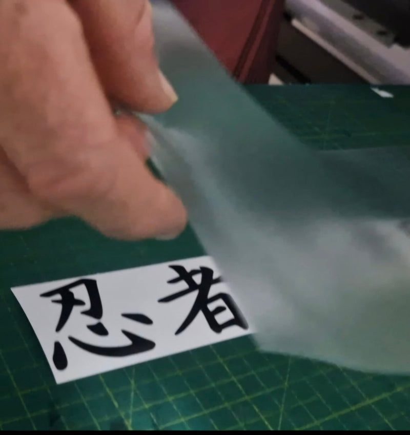Hand holding a piece of translucent material over a sheet with Japanese characters on a green cutting mat.