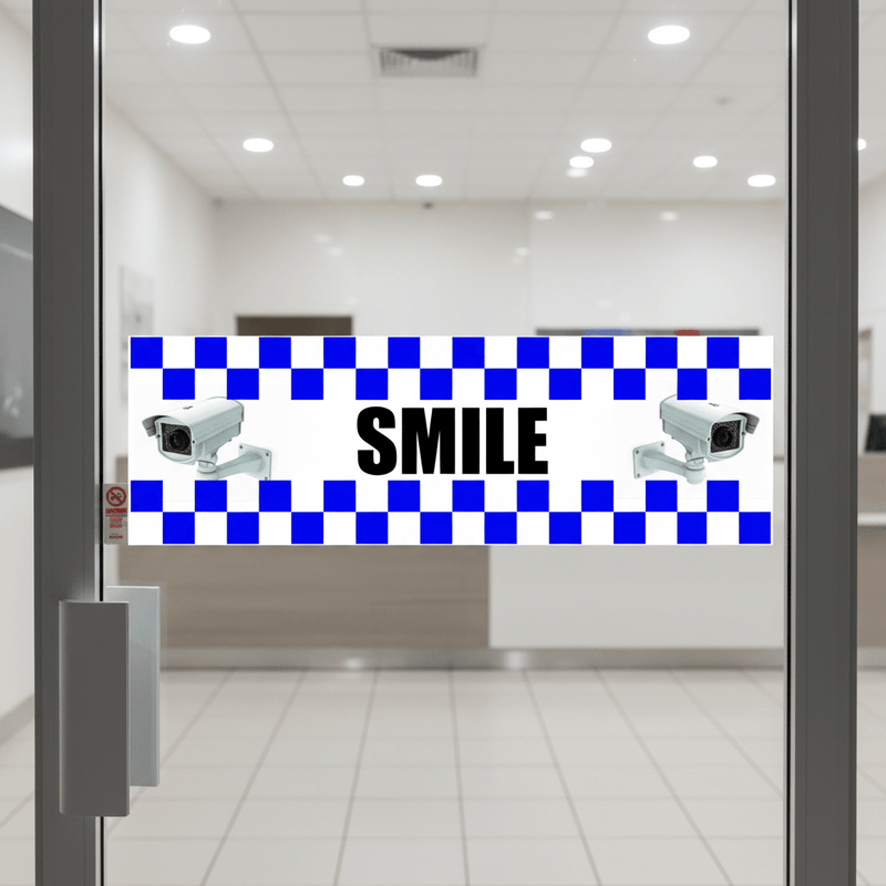 Bold black and white 'SMILE' on camera warning STICKER, applied to a glass commercial entrance door.